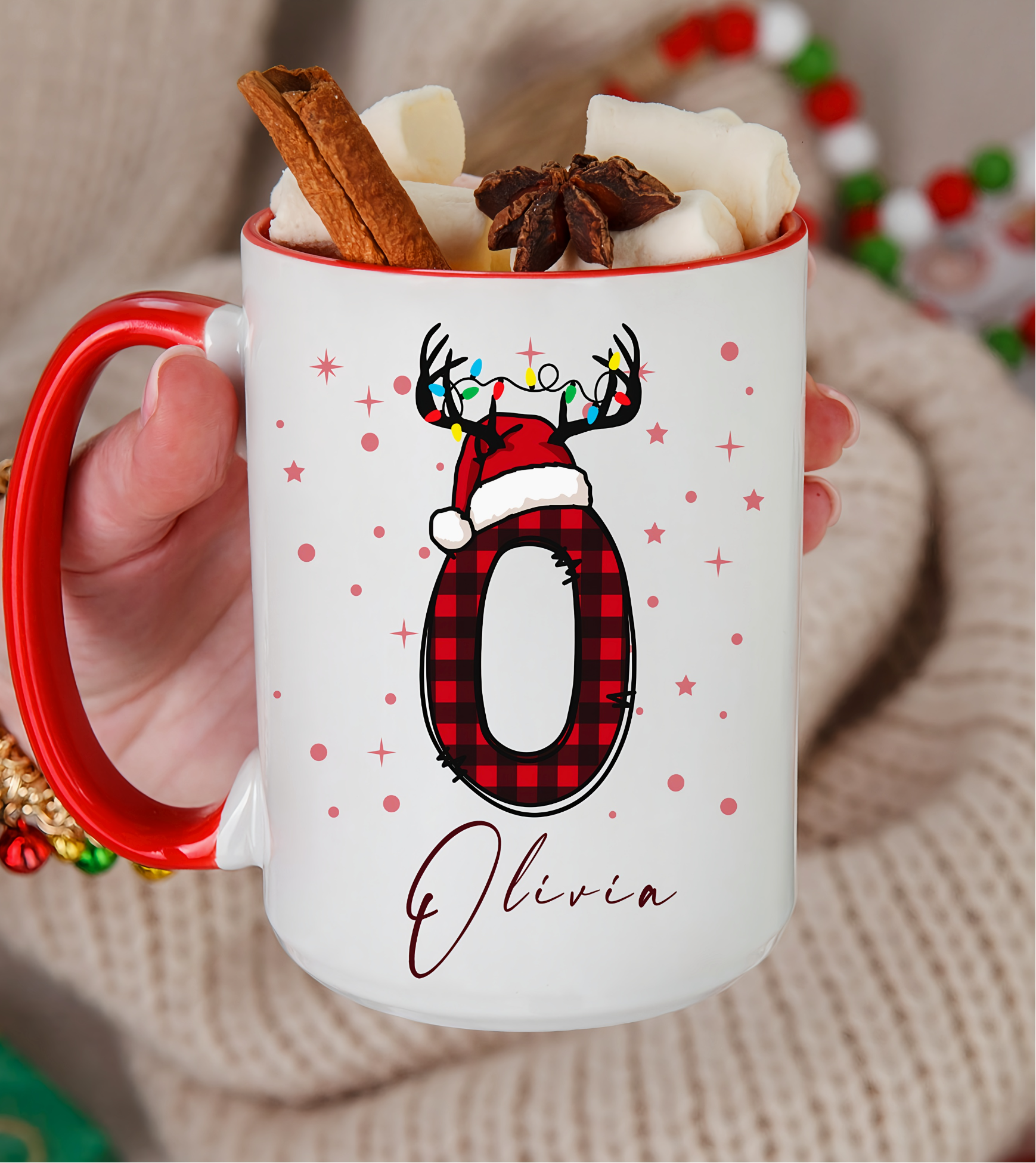 White mug with red handle featuring a reindeer design and the name 'Olivia', filled with hot chocolate and garnishes.